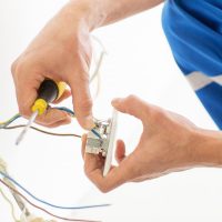 repair, renovation, electricity and people concept - close up of electrician hands with screwdriver fixing socket